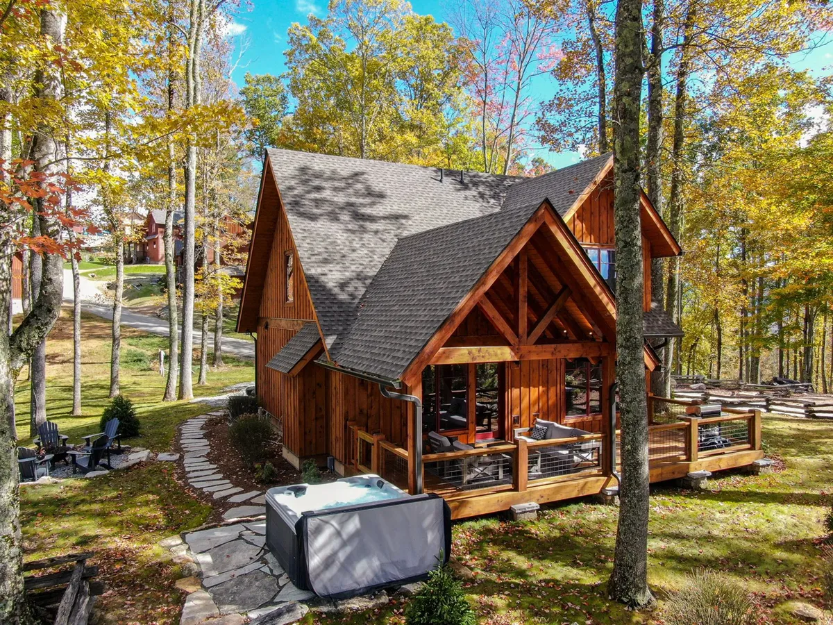 This image showcases the wooden cabin exterior, a generous deck, and the hot tub nestled among surrounding trees. The inviting deck area hints at opportunities for morning coffee, family gatherings, or sunset relaxation, while the hot tub is positioned for privacy and scenic enjoyment.