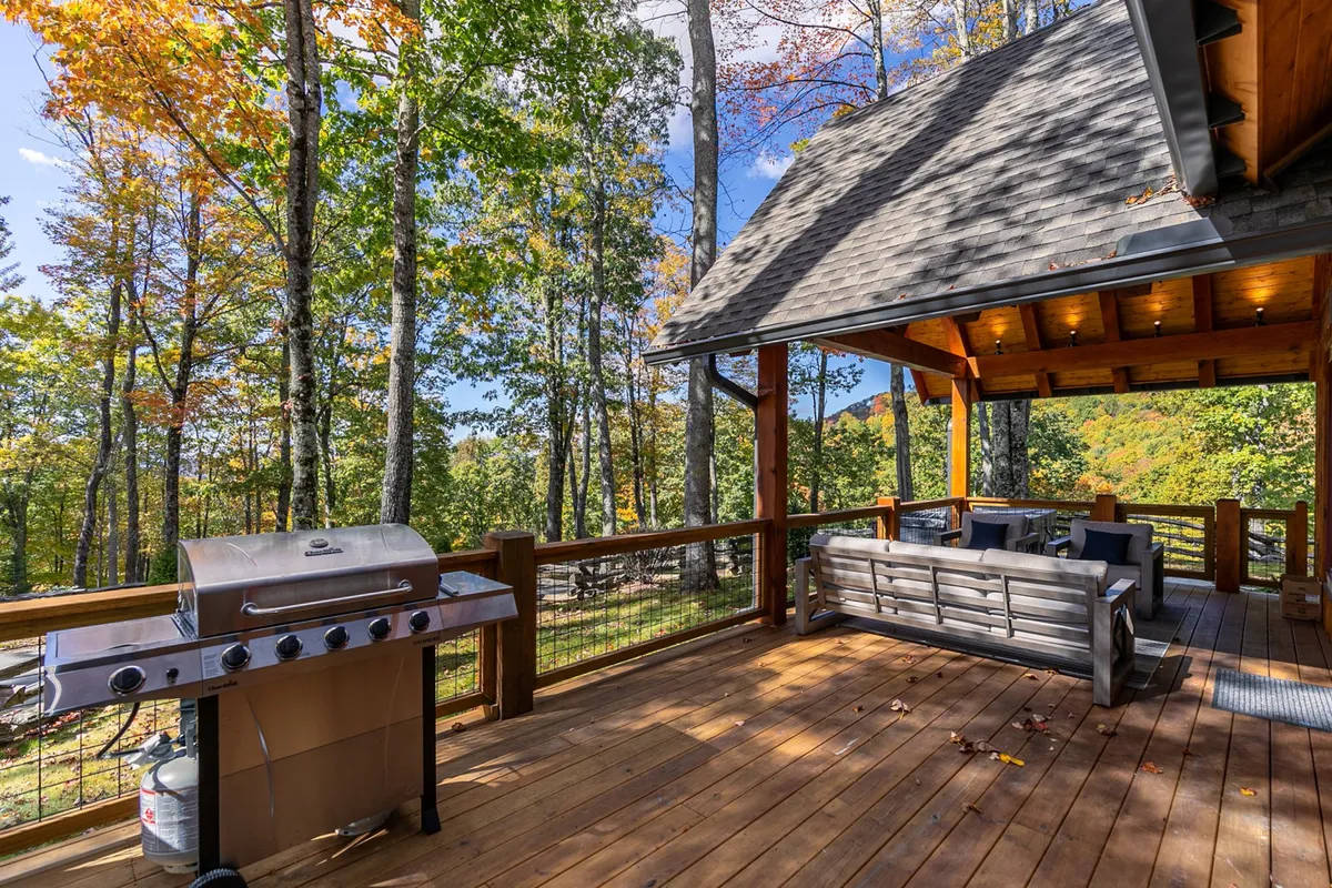This image presents an outdoor seating area with a grill, surrounded by trees. The mood is serene and comfortable, perfect for socializing, dining al fresco, or enjoying the natural surroundings at sunset.