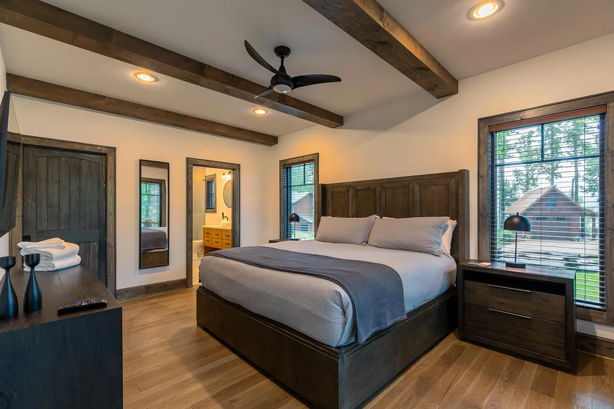 A cozy bedroom featuring a plush bed framed by nightstands, large windows letting in natural light, and a vanity mirror along one wall. The serene atmosphere is perfect for restful evenings and peaceful mornings.
