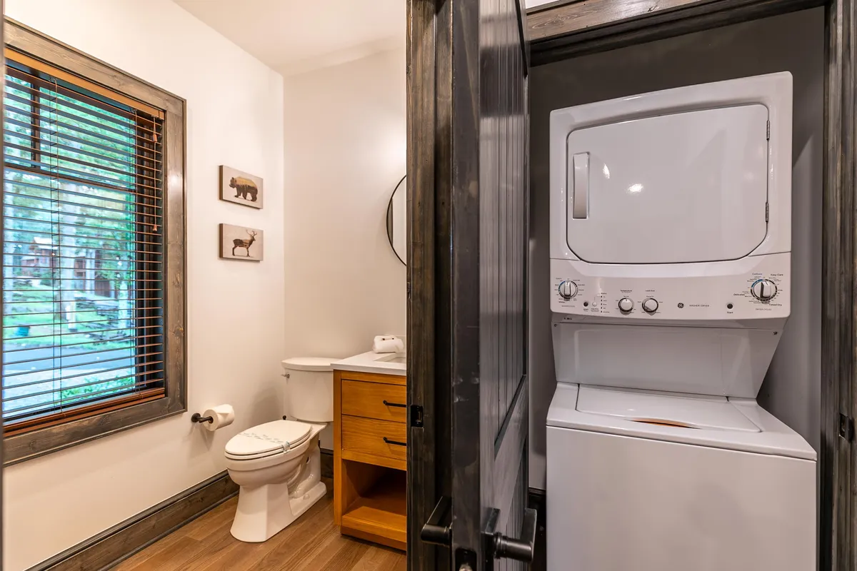 A thoughtfully designed utility area with a washer/dryer, a half bath, wooden cabinetry, and a window letting in natural light. The arrangement prioritizes practicality and comfort, making daily routines convenient for guests and families alike.