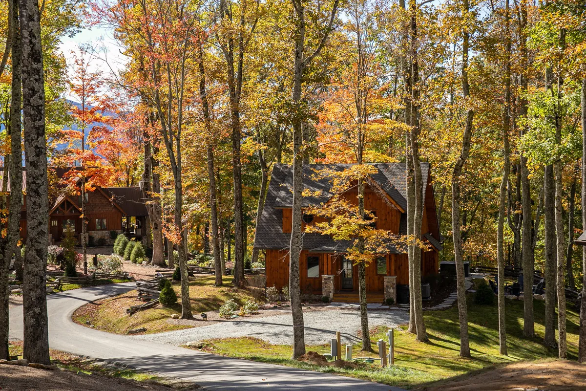 The photo showcases a cozy wooden cabin set among vibrant fall foliage, with a winding driveway leading up to it. The scene conveys a sense of privacy, tranquility, and a strong connection to nature.