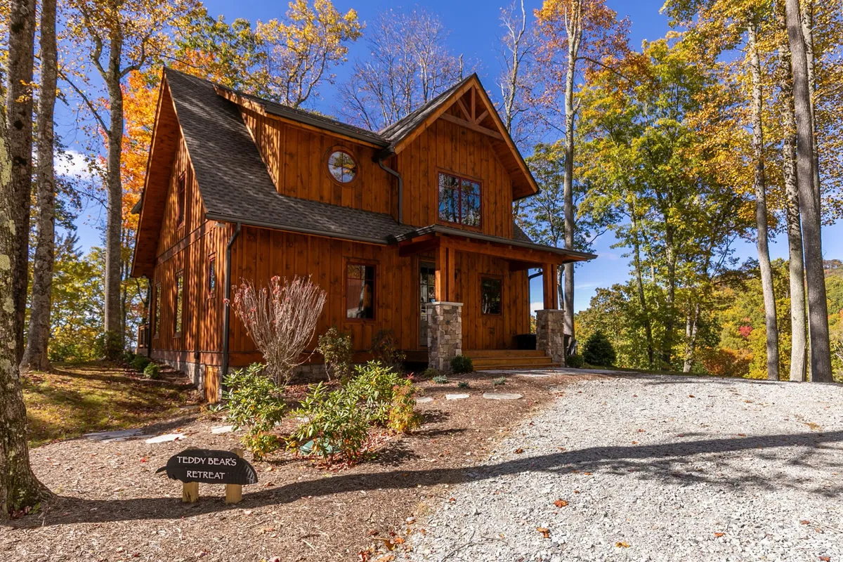 A welcoming exterior of a standalone home featuring a wooden facade, large windows, natural stone accents, and a beautifully landscaped garden. The signage denotes the property as part of the Eagles Nest community. People can be seen relaxing on the porch, enjoying nature walks, and gathering around a fire pit, with the surrounding trails inviting further exploration.