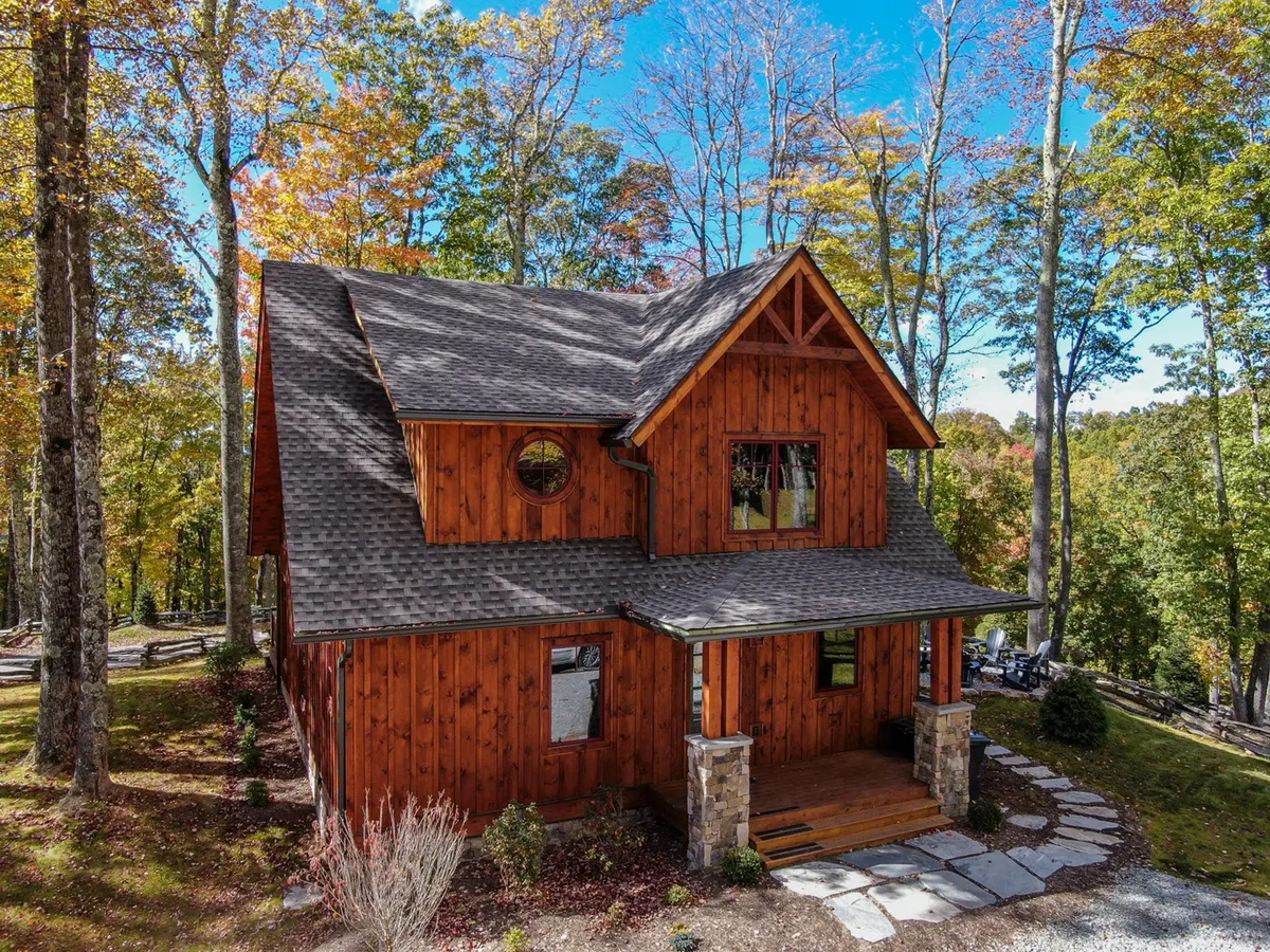 A cozy wooden exterior with a unique circular window and stone steps, set against a wooded backdrop. The porch invites moments of relaxation, while the peaceful setting hints at year-round enjoyment, from golden sunsets to cool evenings by the fire.